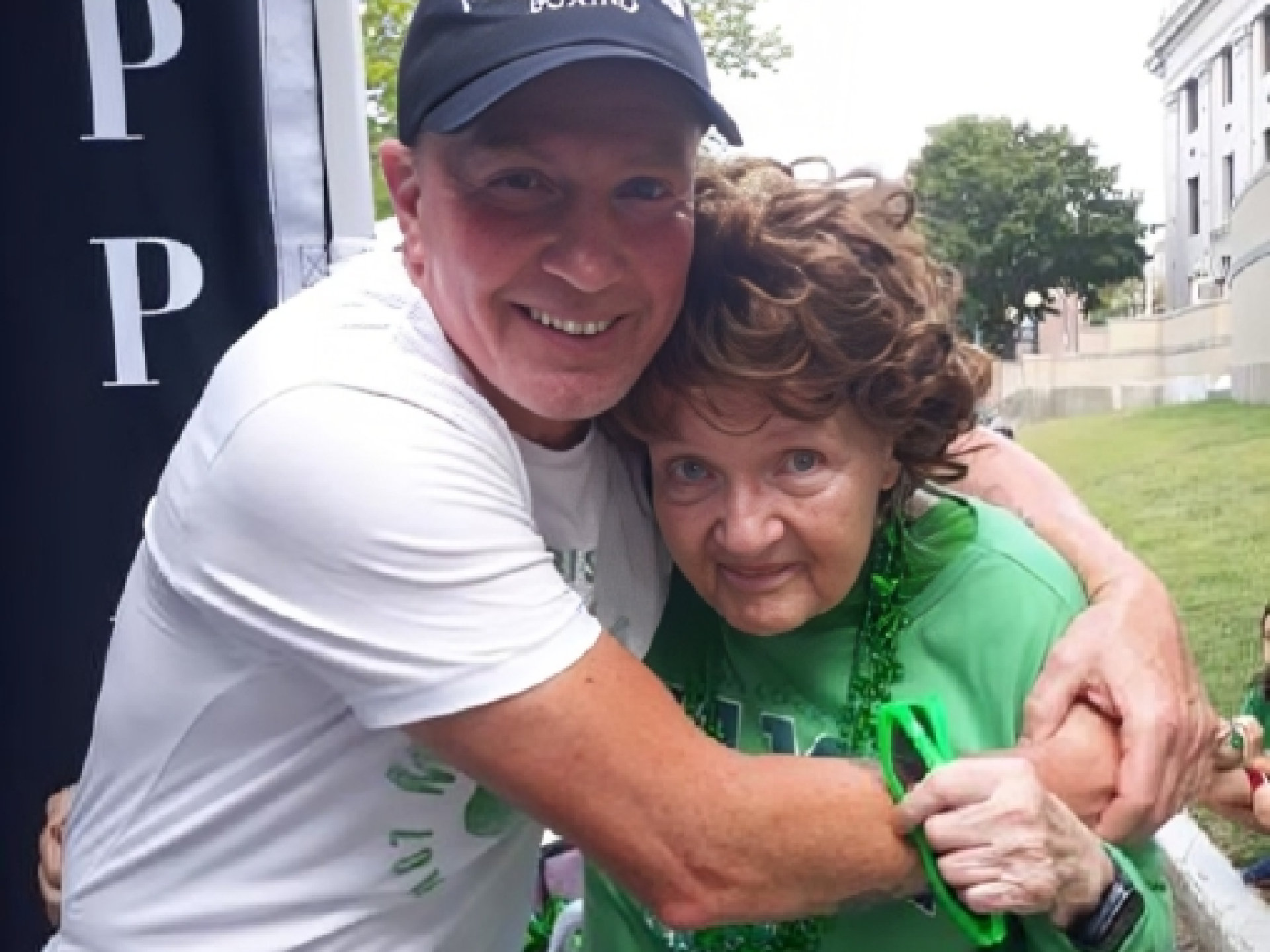 A man smiles and hugs an elderly woman dressed in green.